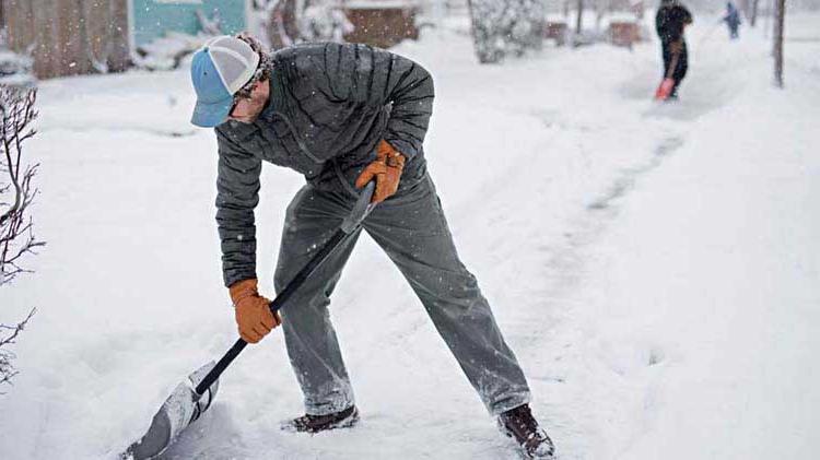Business owner shoveling snow to clear a sidewalk in order to prevent slip 和 falls in the workplace.